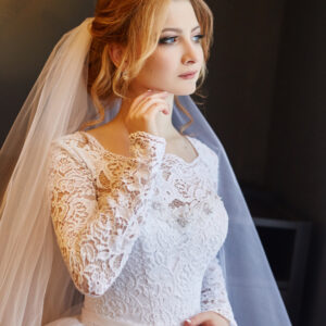 Portrait of a bride in a chic white wedding dress preparing for the wedding ceremony. Portrait of a blonde woman near a window in a white dress and a veil on her head. Bride is waiting for her groom