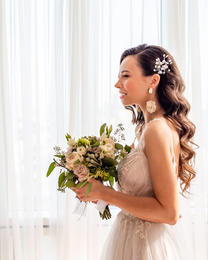 Beautiful bride with wedding flowers bouquet in wedding dress. Bride with wedding makeup and hairstyle in hotel